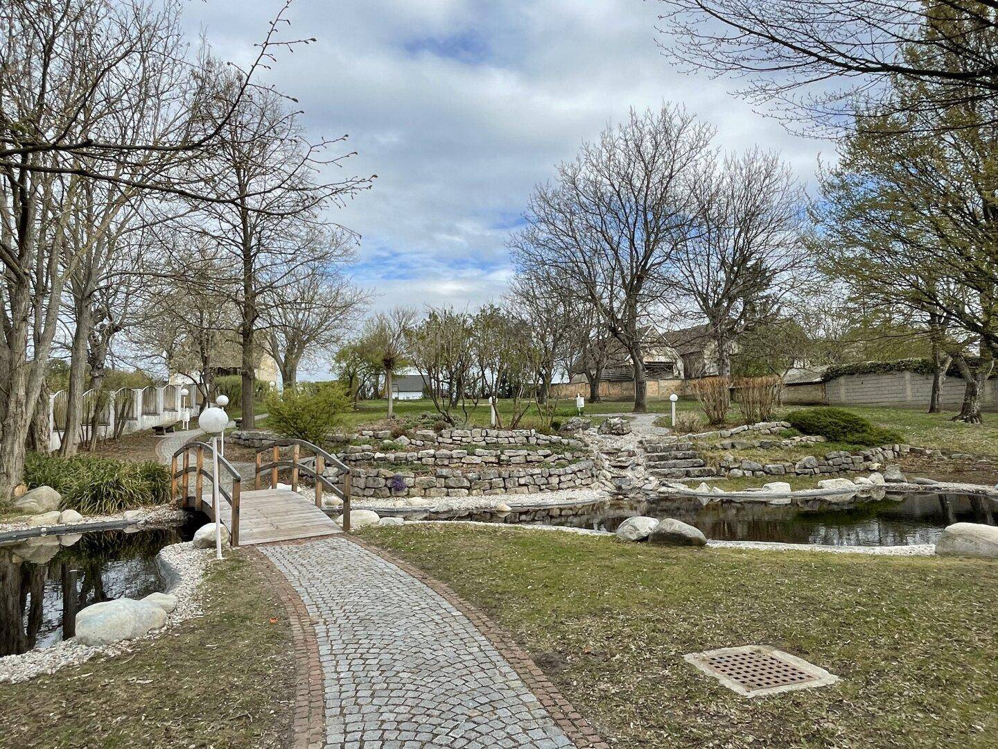 Gepflegter Gartenbereich mit einem kleinen Teich, einer Holzbrücke und dekorativen Steinelementen.