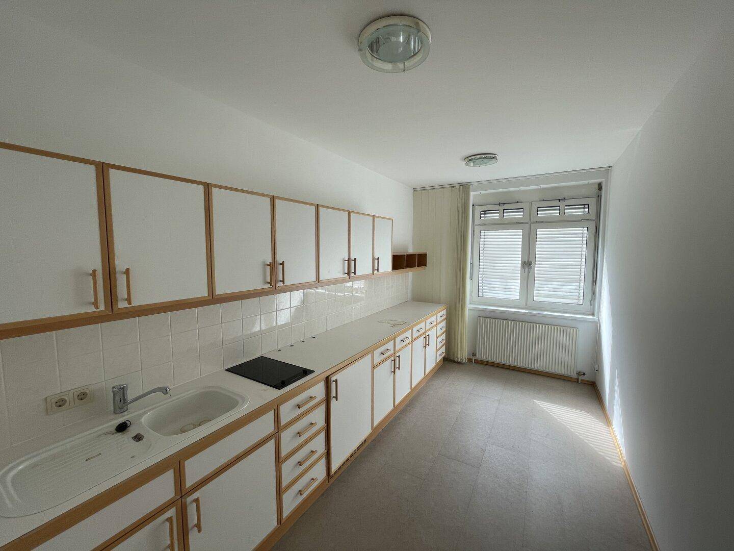 Funktionale Küche mit weißen Schränken, integriertem Kochfeld und einem Fenster mit Jalousien.