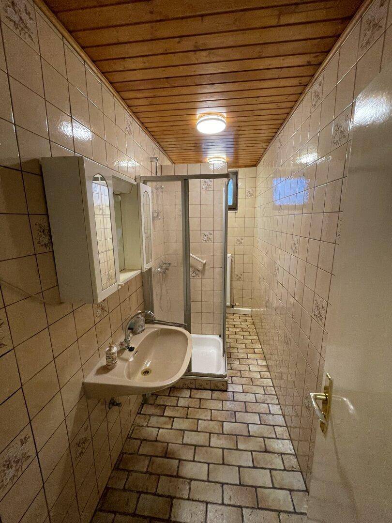 Schmaler Duschraum mit Fliesenboden, Holzdecke und einfacher Ausstattung.