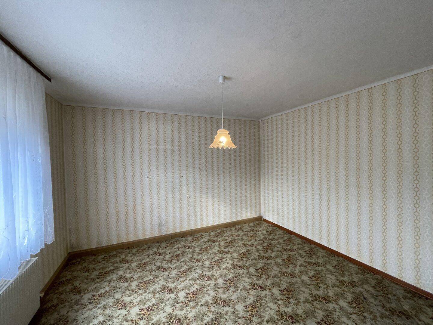 Leeres Zimmer mit Teppichboden und gestreifter Tapete, ideal für eine Neugestaltung.