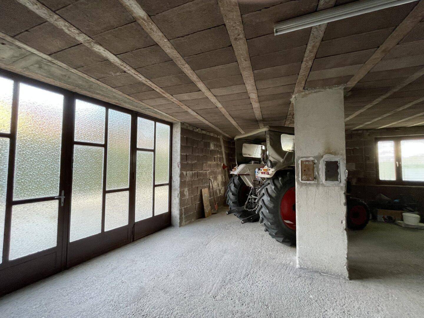 Großer Garagenraum mit Betonboden, hohen Decken und einem Traktor.