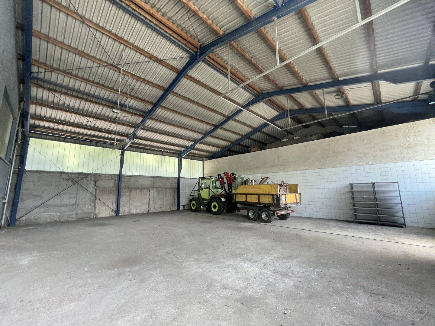 Geräumige Lagerhalle mit hoher Decke, sichtbarer Dachkonstruktion und Betonboden, inklusive Arbeitsgerät.