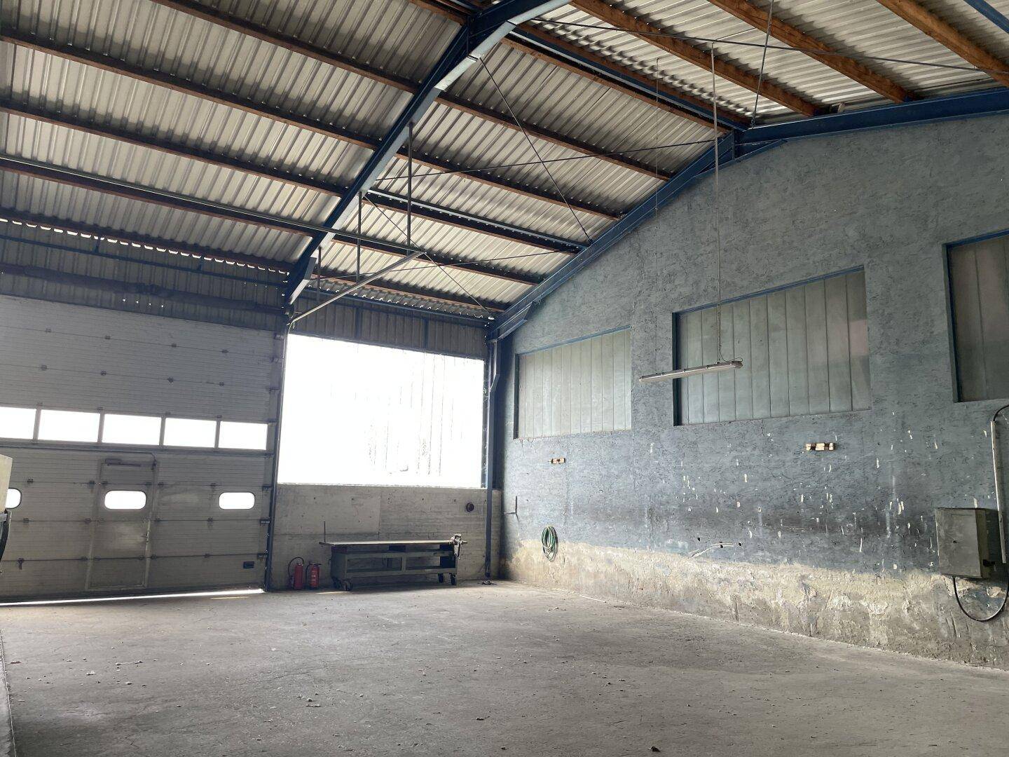 Innenansicht der Lagerhalle mit großem Rolltor, Werkbank und viel Tageslichteinfall.