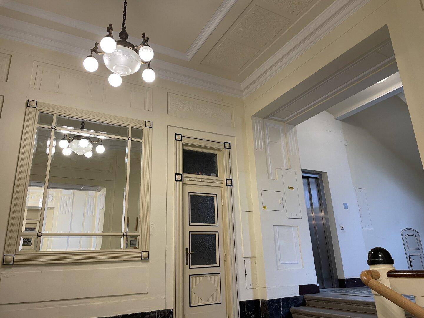 Eleganter Hausflur mit Spiegel, dekorativen Elementen und sichtbarem Aufzug.