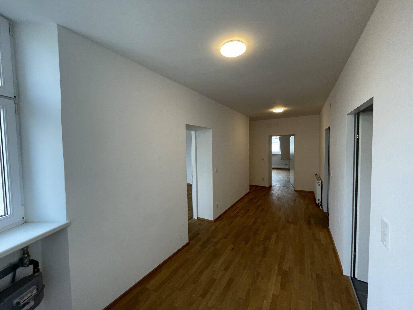 Langer Flur mit Parkettboden, weißen Wänden und Zugang zu verschiedenen Zimmern.