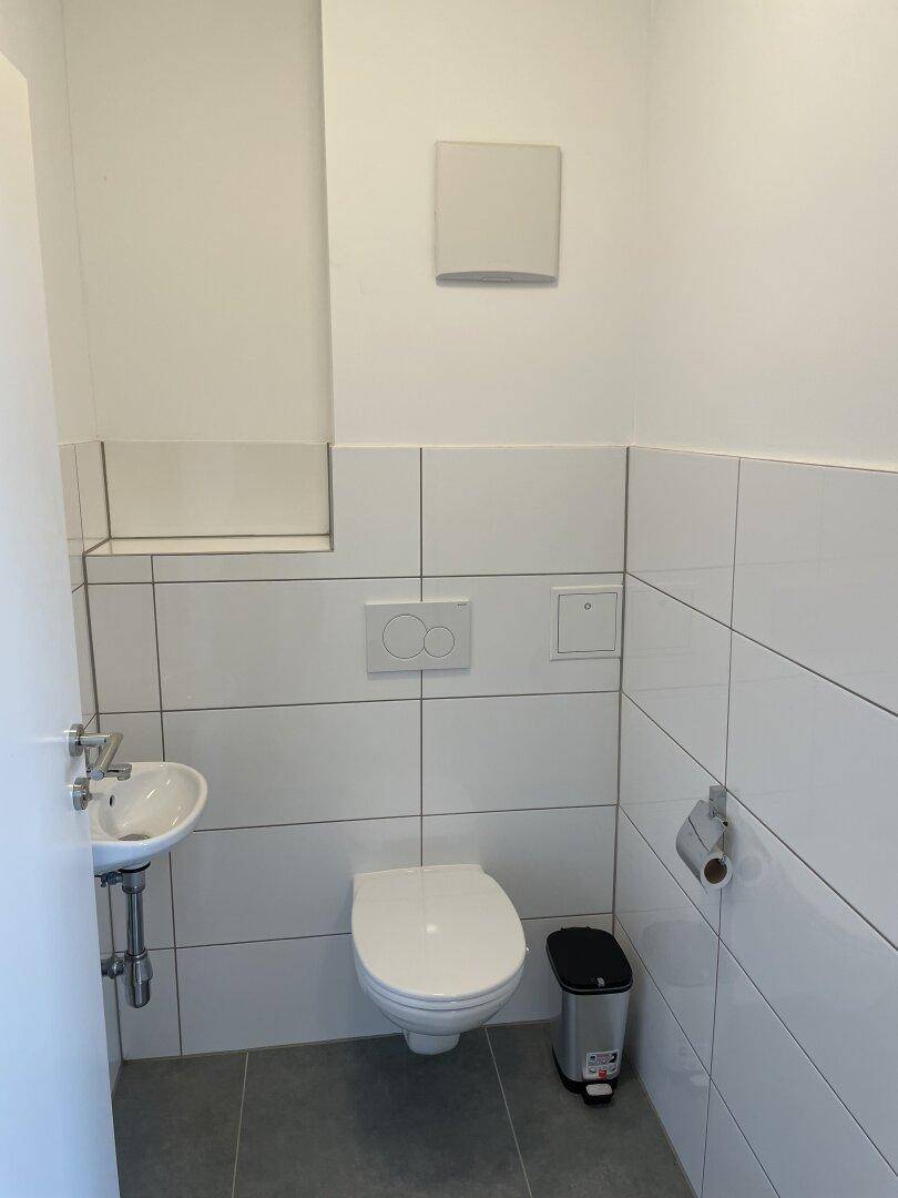 Modernes Gäste-WC mit weißen Fliesen, wandhängendem WC und kleinem Waschbecken.