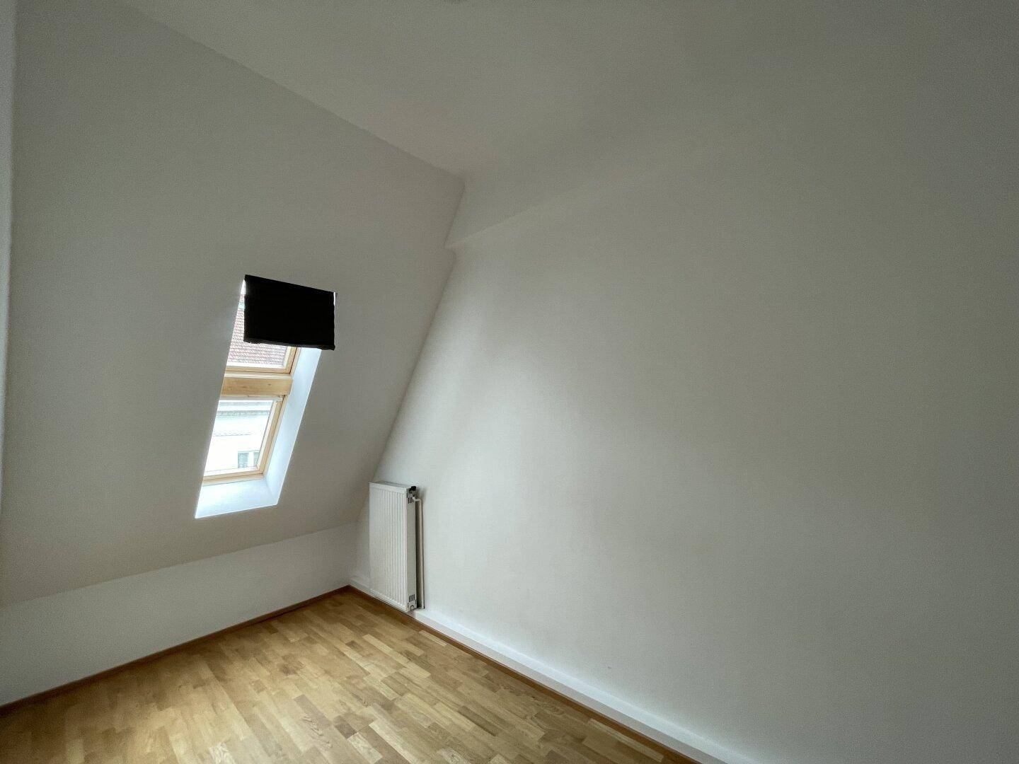 Dachzimmer mit Parkettboden, weißen Wänden und einem Dachfenster für natürliches Licht.