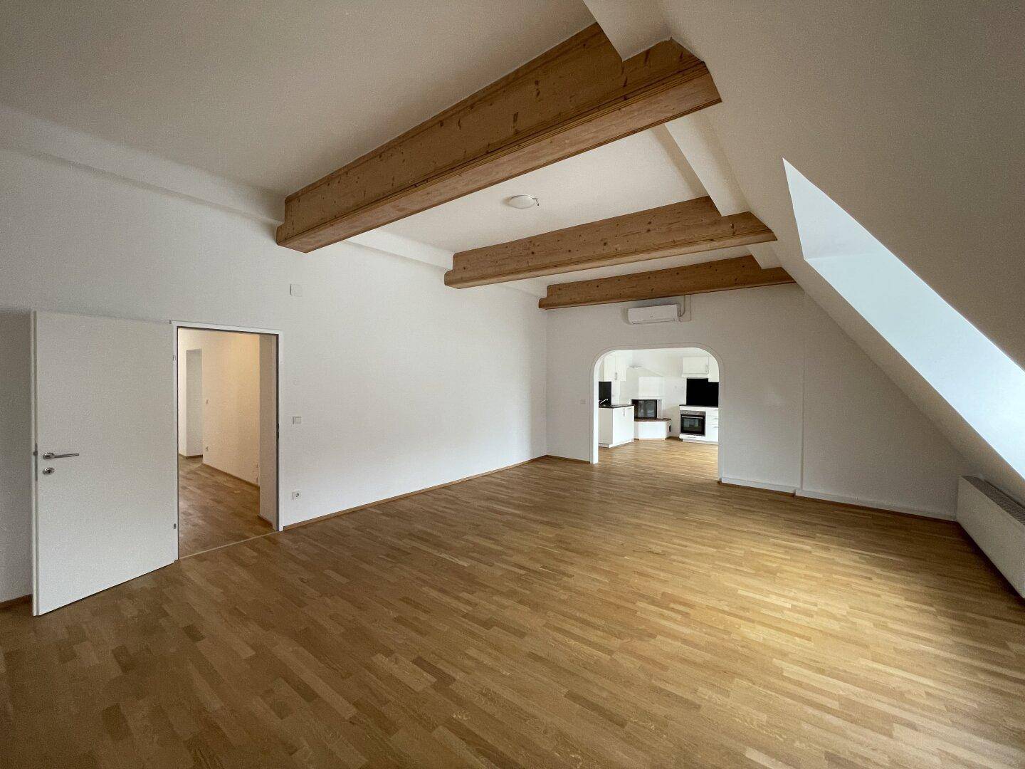 Geräumiger Wohnbereich mit Holzbalken, Parkettboden und offener Verbindung zu weiteren Räumen.