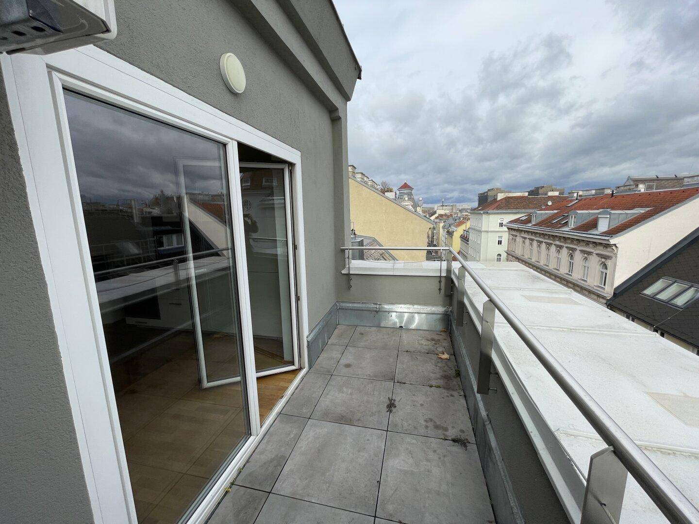 Kleiner Balkon mit Fliesenboden und Blick über die Dächer der Stadt.