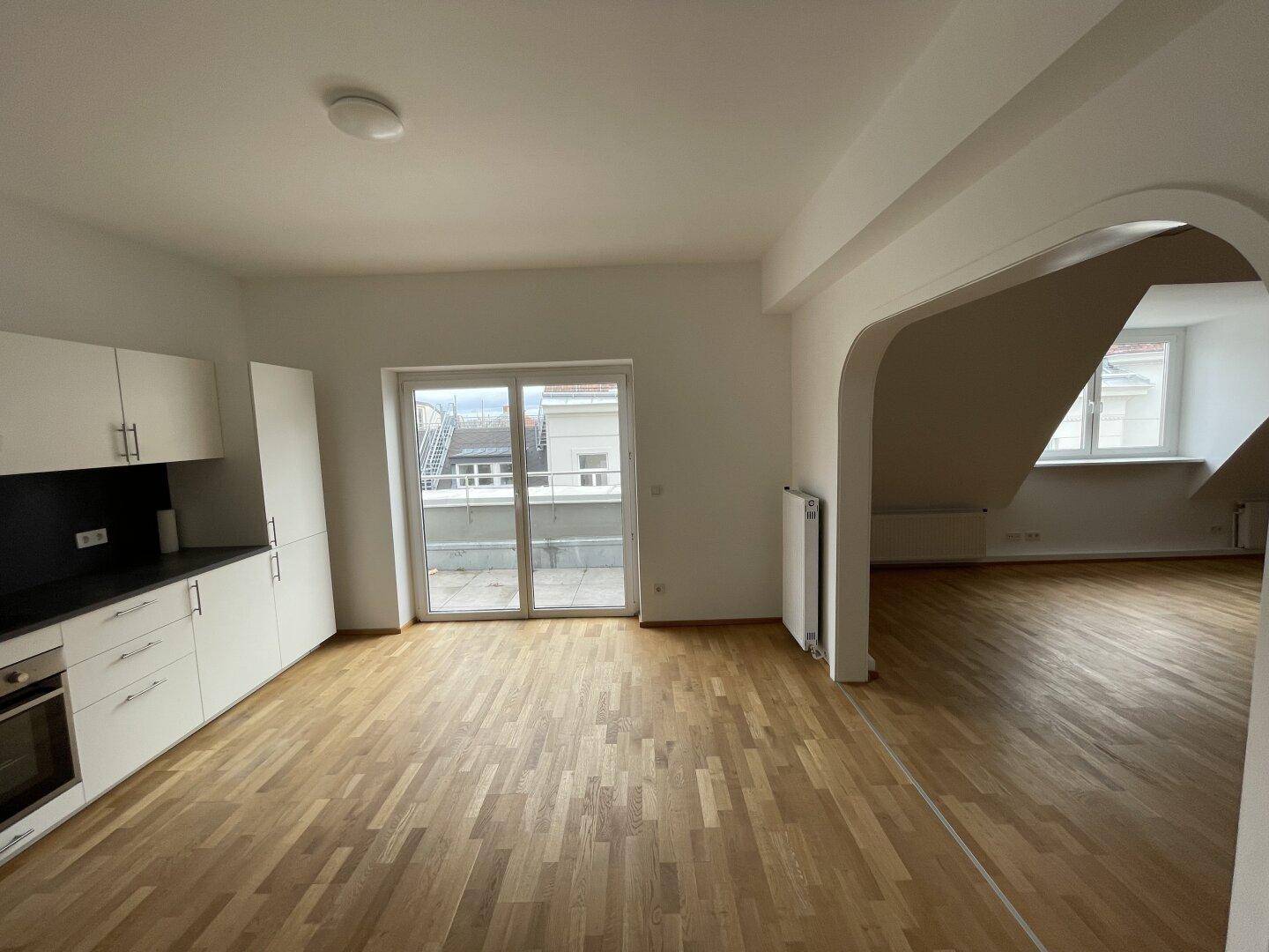 Moderne Küche mit weißen Schränken, Parkettboden und Zugang zu einem Balkon.