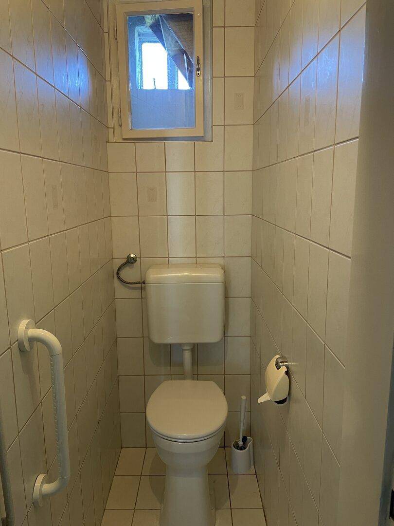 Kleines WC mit Toilette, Fliesen und Fenster.