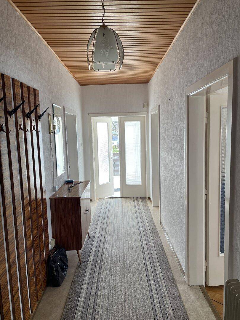 Langer Flur mit Holzdecke, Teppich und Garderobe.
