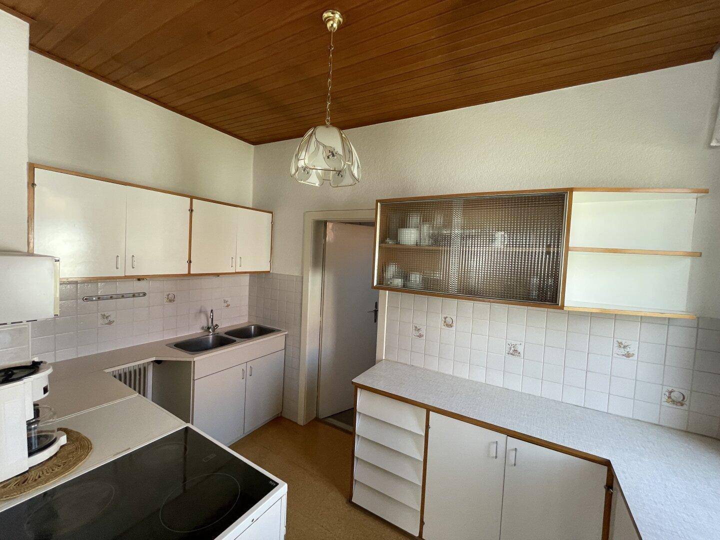Einfache Küche mit weißen Schränken, Doppelspüle und Holzdecke.
