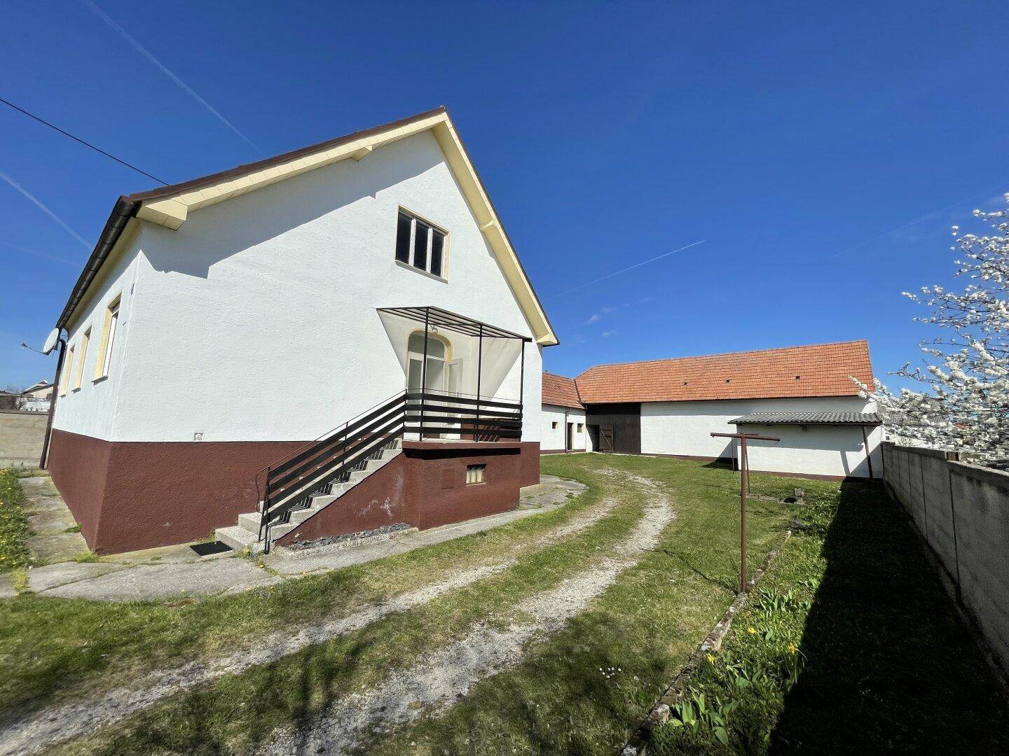Ländliches Anwesen mit weißem Haus, braunem Sockel und großem Grundstück unter blauem Himmel.