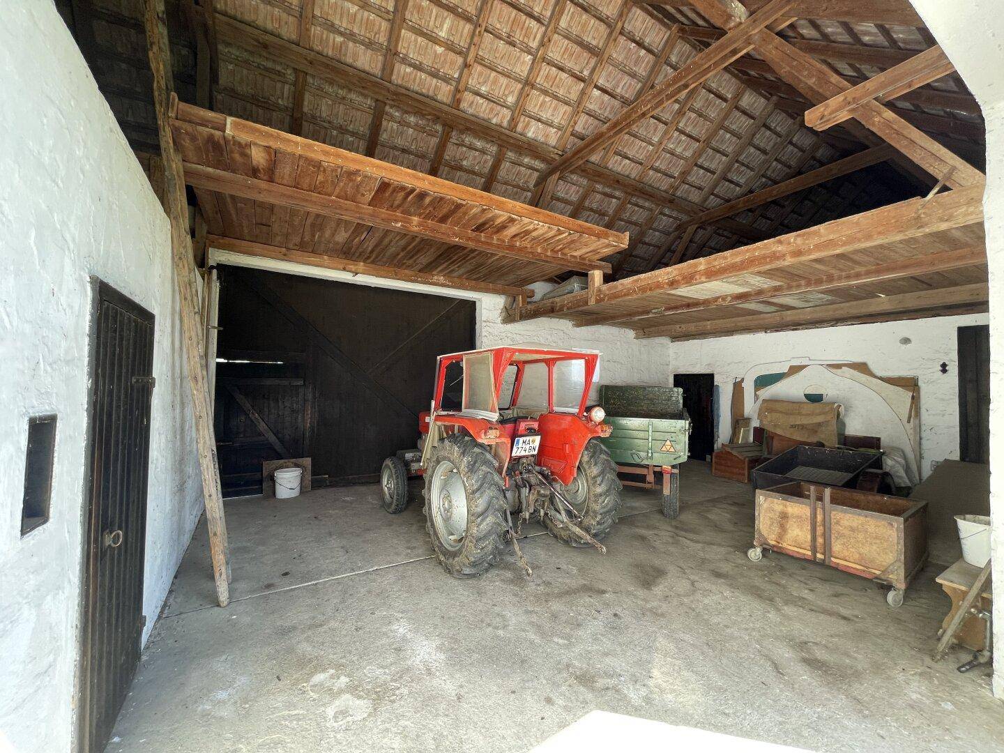 Geräumige Scheune mit Holzdachstuhl, Betonboden und einem Traktor.