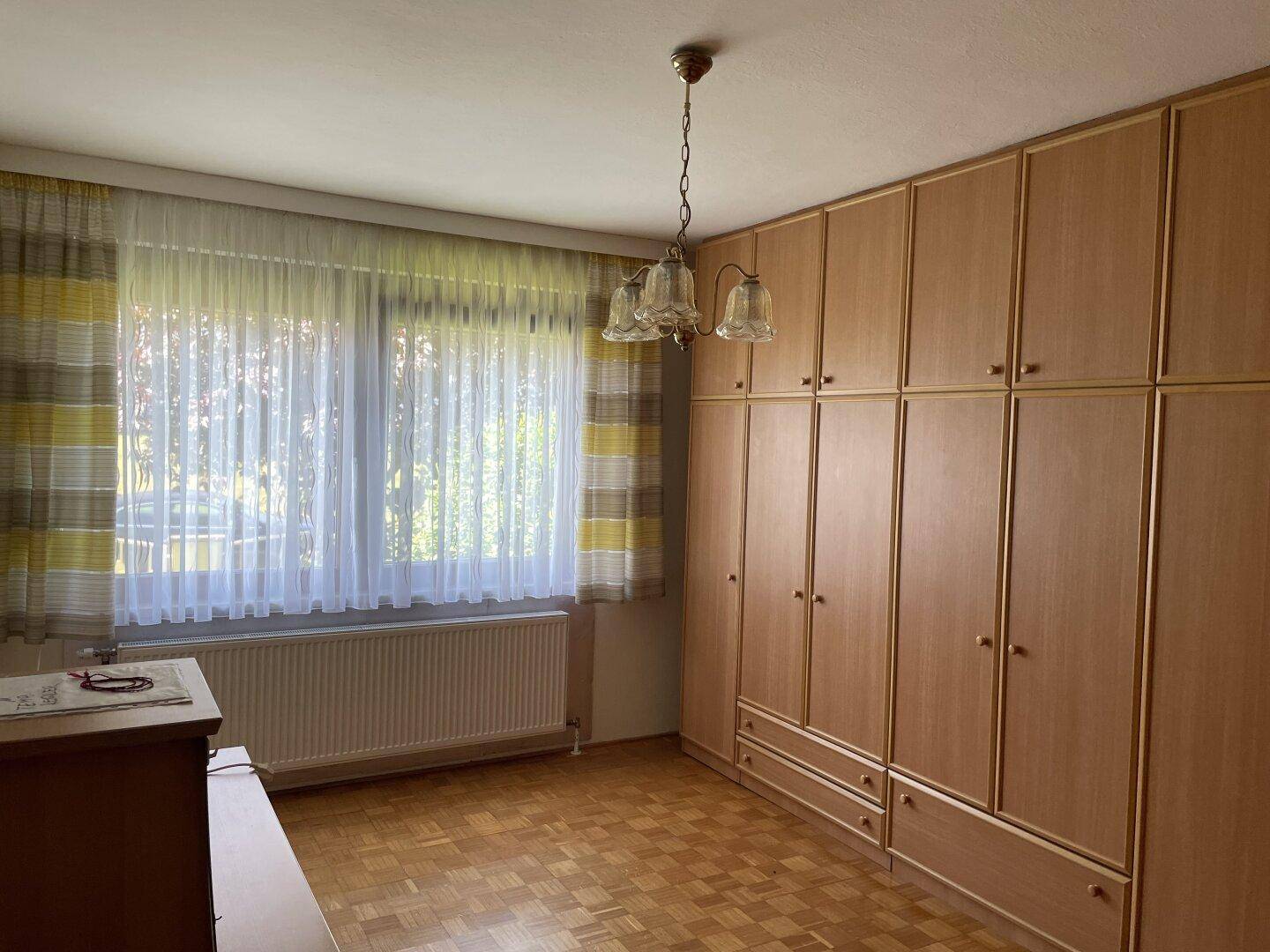 Schlafzimmer mit Einbauschränken, Parkettboden und Blick in den Garten.