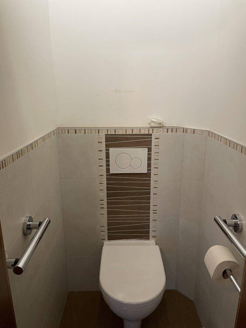 Kleines Gäste-WC mit Wand-WC, Fliesen und praktischen Haltegriffen.