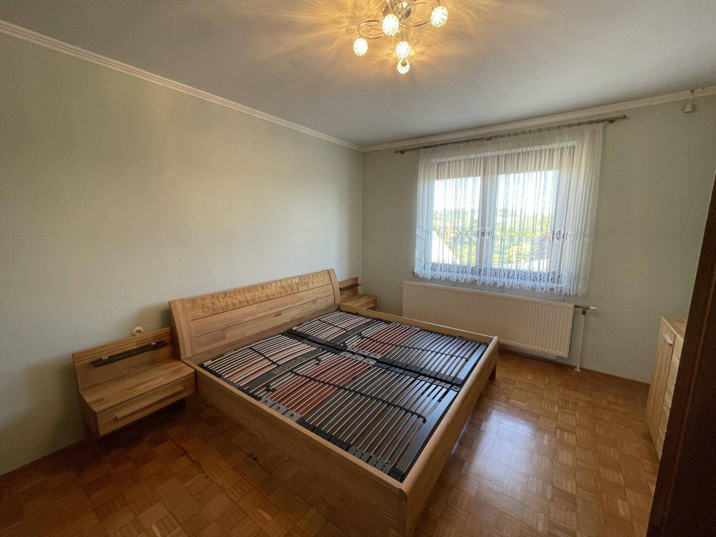 Helles Schlafzimmer mit Holzbett, Parkettboden und großem Fenster.