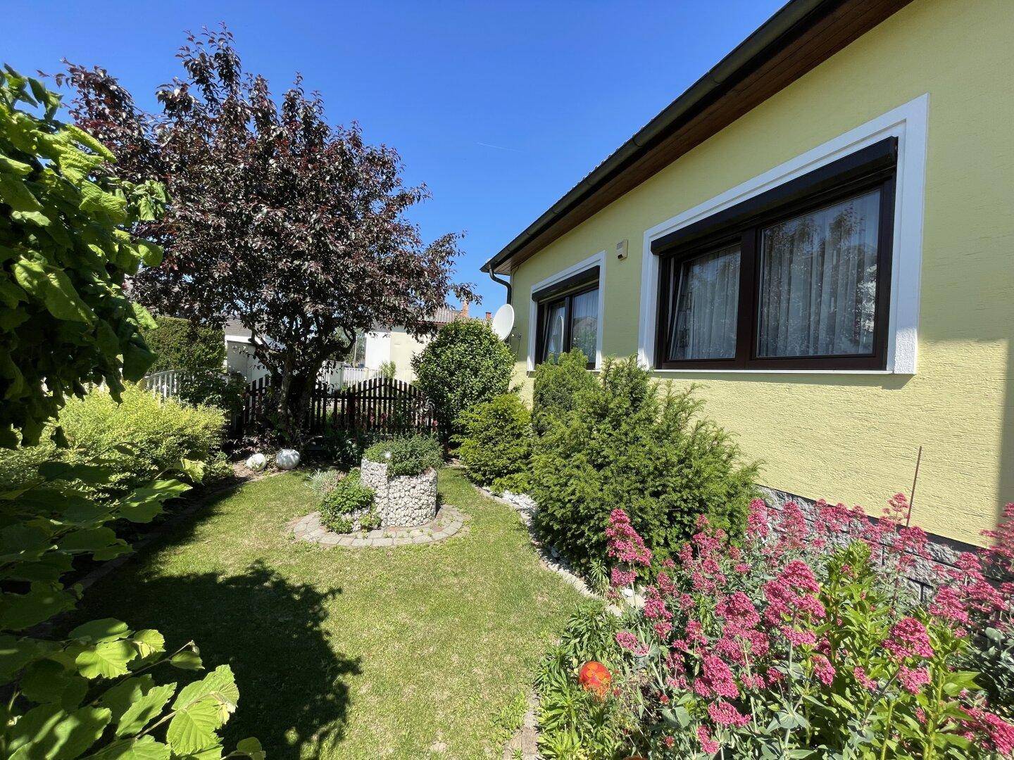 Seitlicher Gartenbereich mit Rasen, Blumenbeeten und Blick auf die Hausfassade.