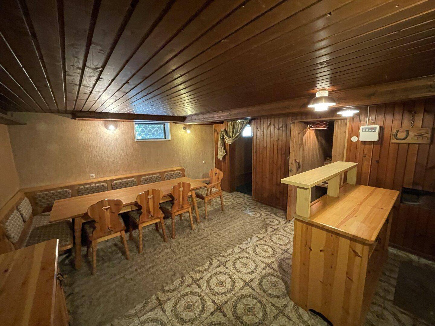 Rustikaler Partyraum im Keller mit Holztäfelung, langer Tafel und Bar.