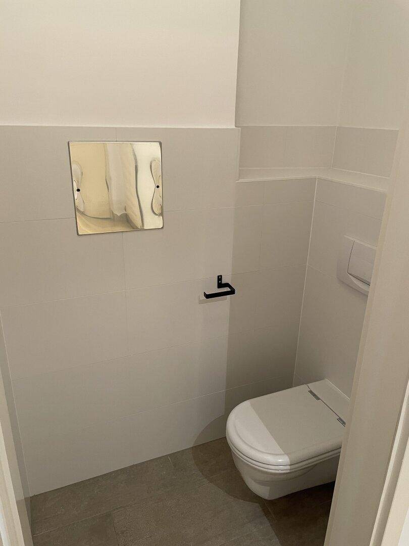 Separates WC mit wandhängender Toilette und hellen Fliesen, funktional und sauber.
