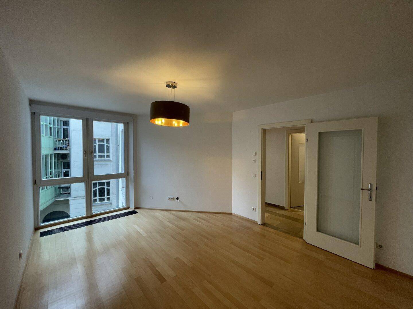Gemütliches Wohnzimmer mit Parkettboden und großen Fenstern, die viel Licht hereinlassen.