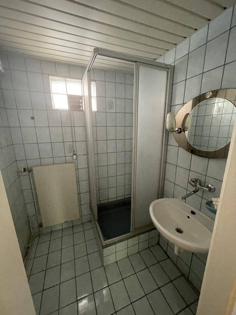 Badezimmer mit blauen Fliesen, Duschkabine, Waschbecken und einem kleinen Fenster.