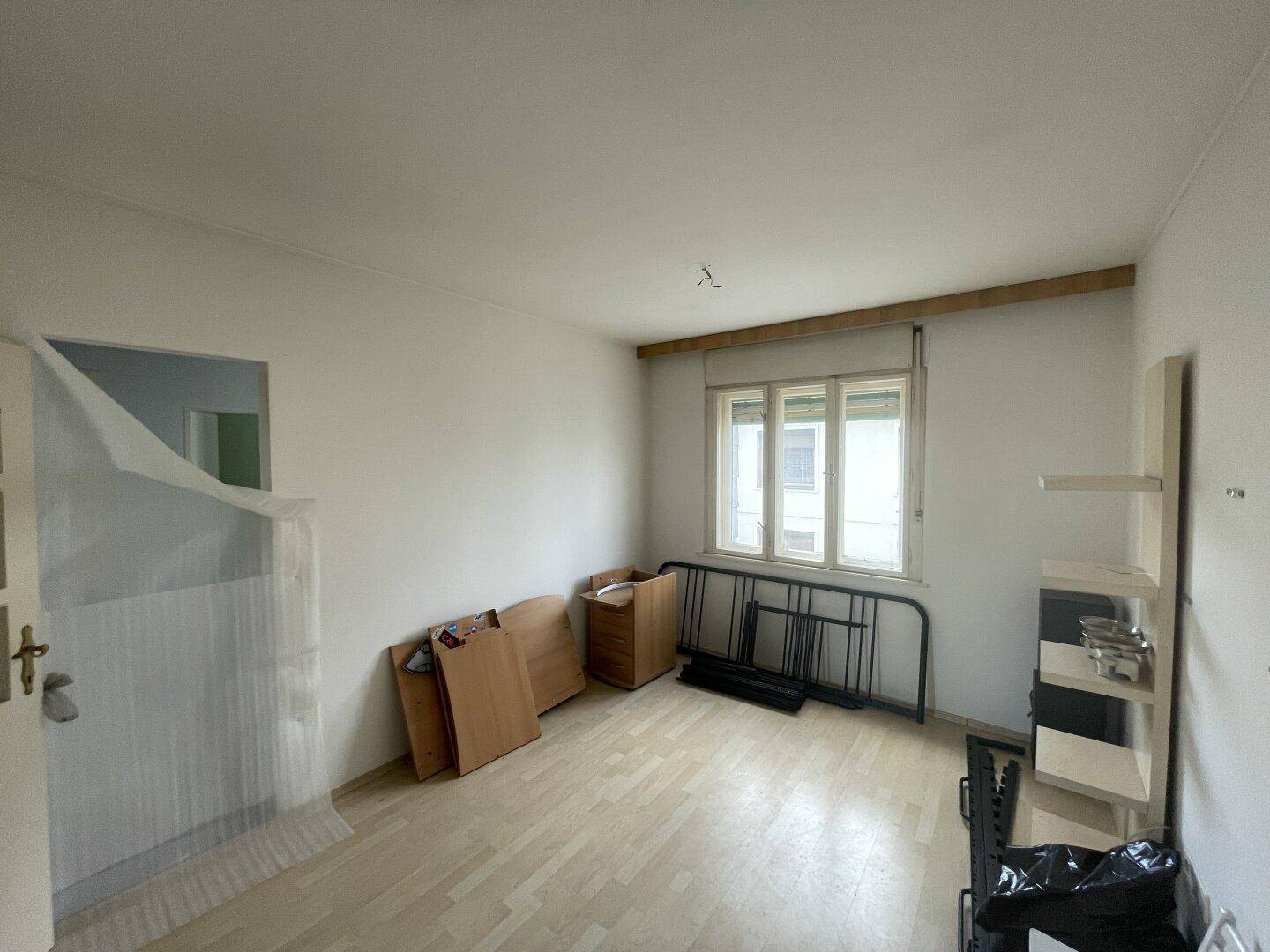 Schlafzimmer mit Laminatboden, weißen Wänden und einem Fenster, das viel Licht hereinlässt.