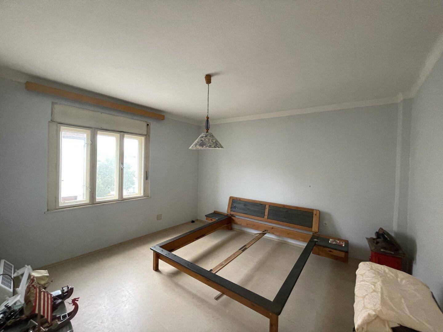 Schlafzimmer mit Laminatboden, einem Bettgestell und einem Fenster für natürliche Belichtung.