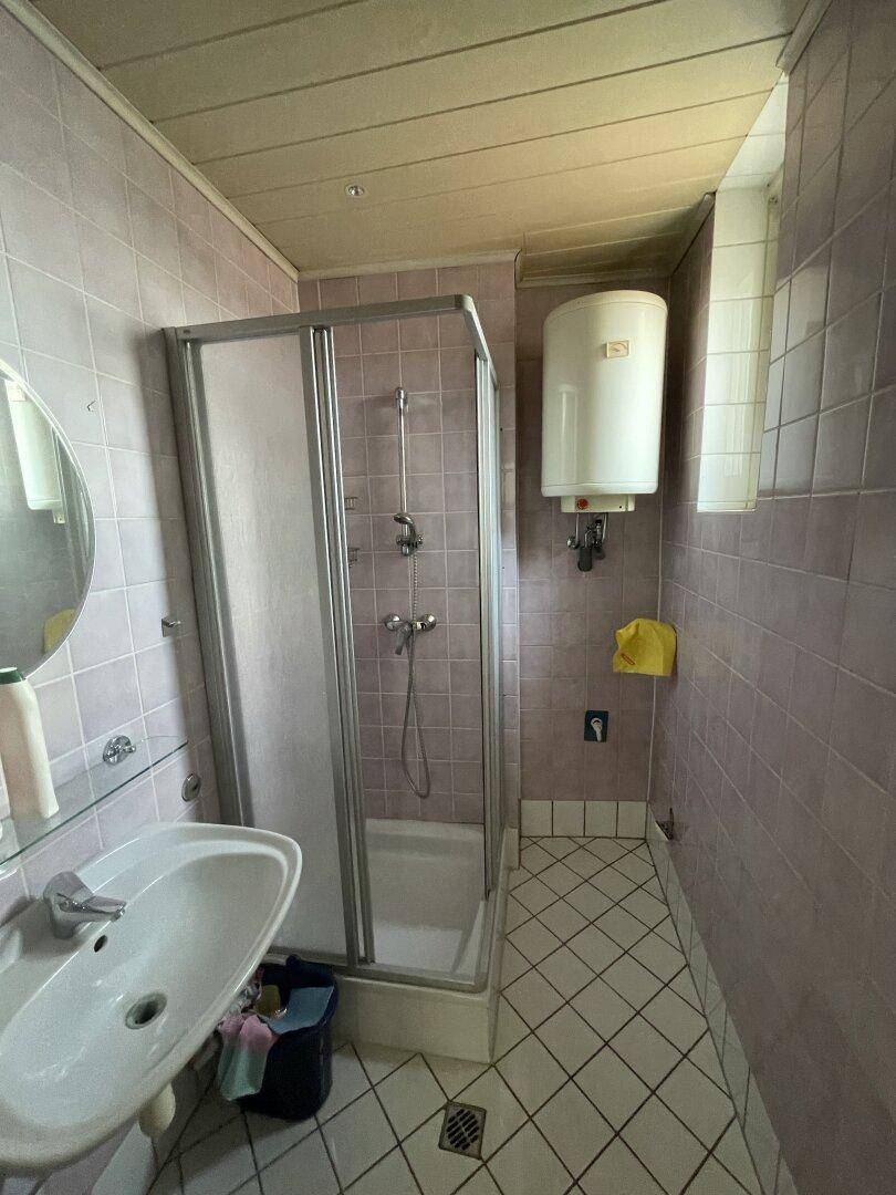Badezimmer mit rosa Fliesen, Duschkabine, Waschbecken und einem Warmwasserboiler.