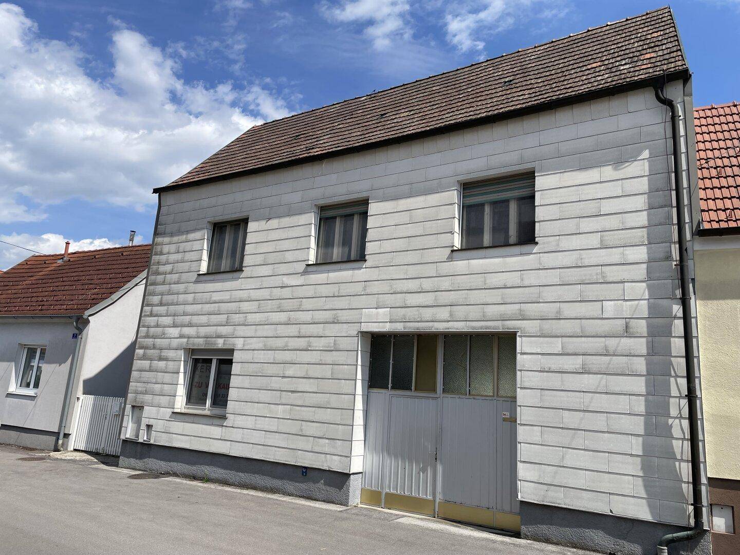 Fassade eines Wohnhauses mit weißer Verkleidung, mehreren Fenstern und einem Garagentor.