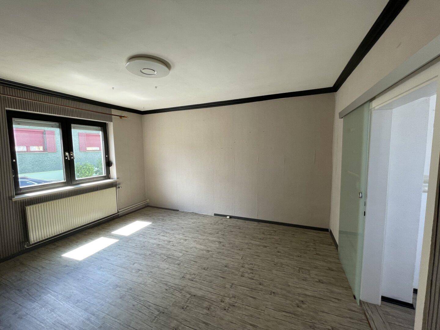 Helles Wohnzimmer mit Laminatboden und Schiebetür zu einem weiteren Raum.