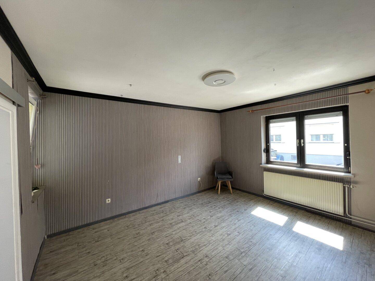 Geräumiges Zimmer mit Laminatboden, gestreiften Tapeten und großem Fenster.