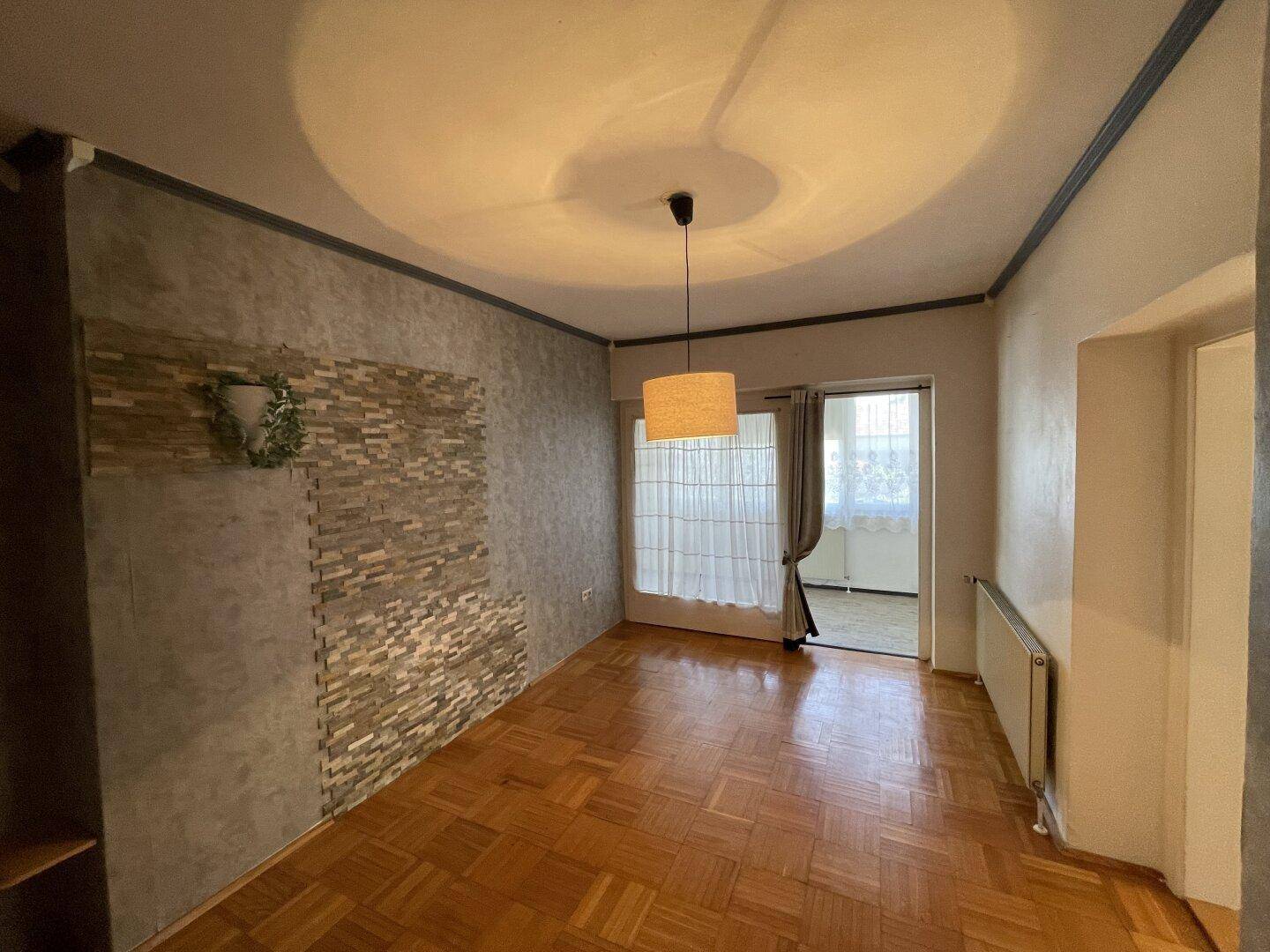 Gemütliches Wohnzimmer mit Parkettboden, dekorativer Wand und Zugang zum Balkon.