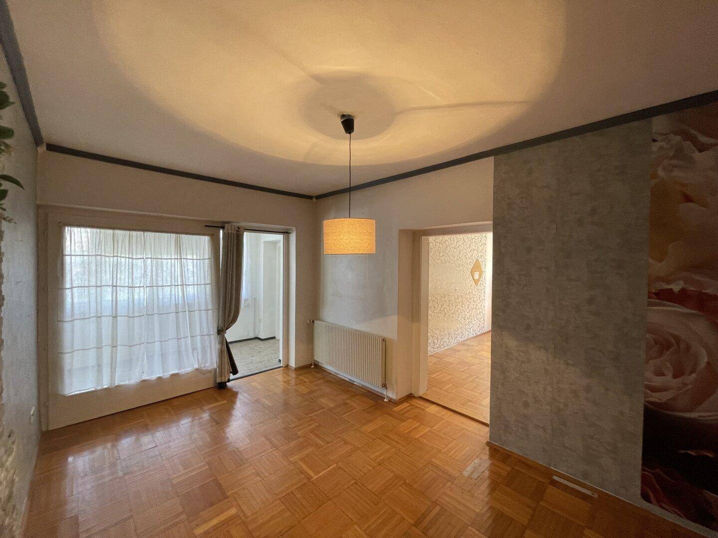 Wohnzimmer mit Parkettboden, Pendelleuchte und Blick in angrenzende Räume.