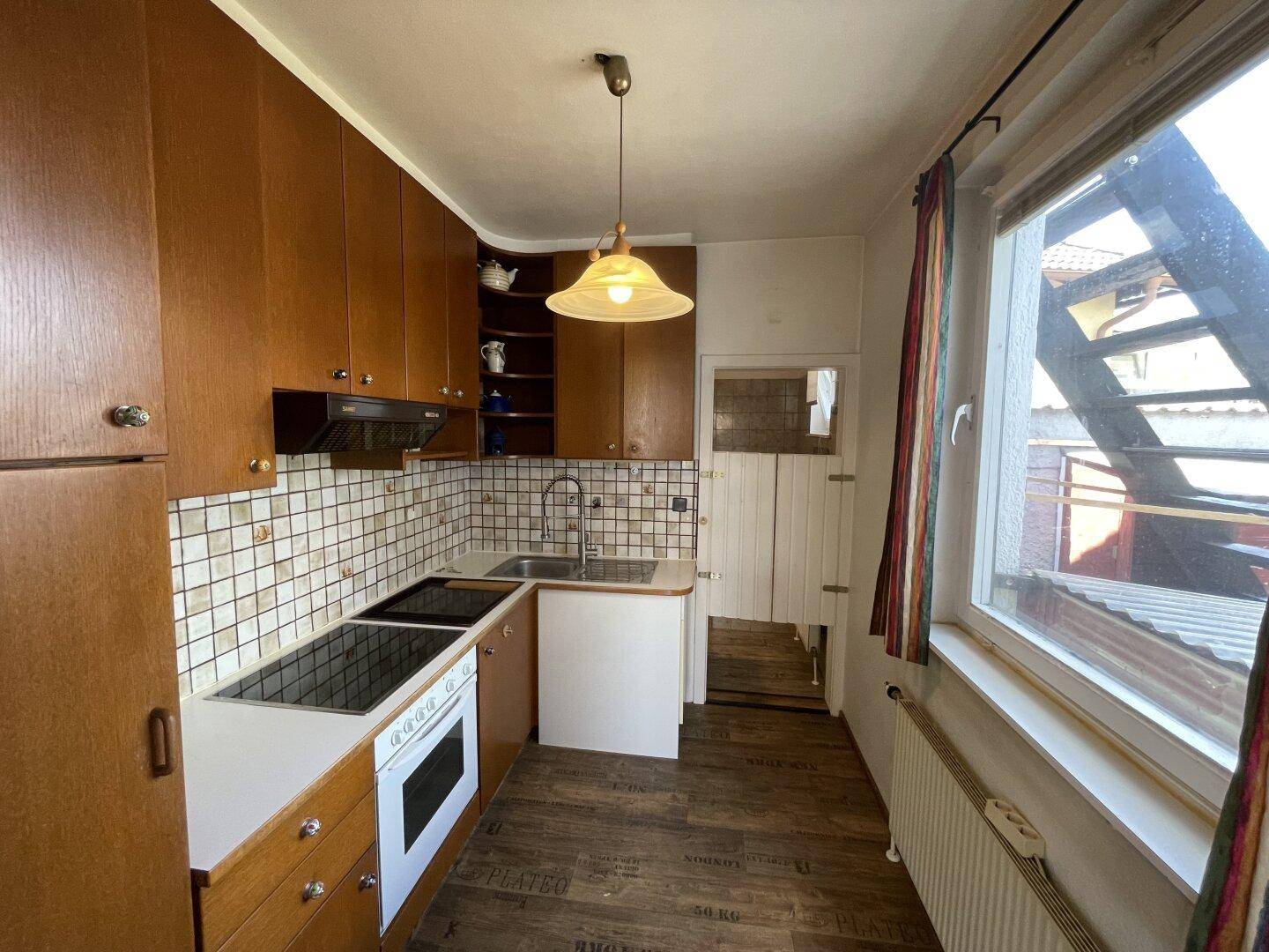 Funktionale Küche mit Holzschränken, Fliesenrückwand und Fenster mit Ausblick.