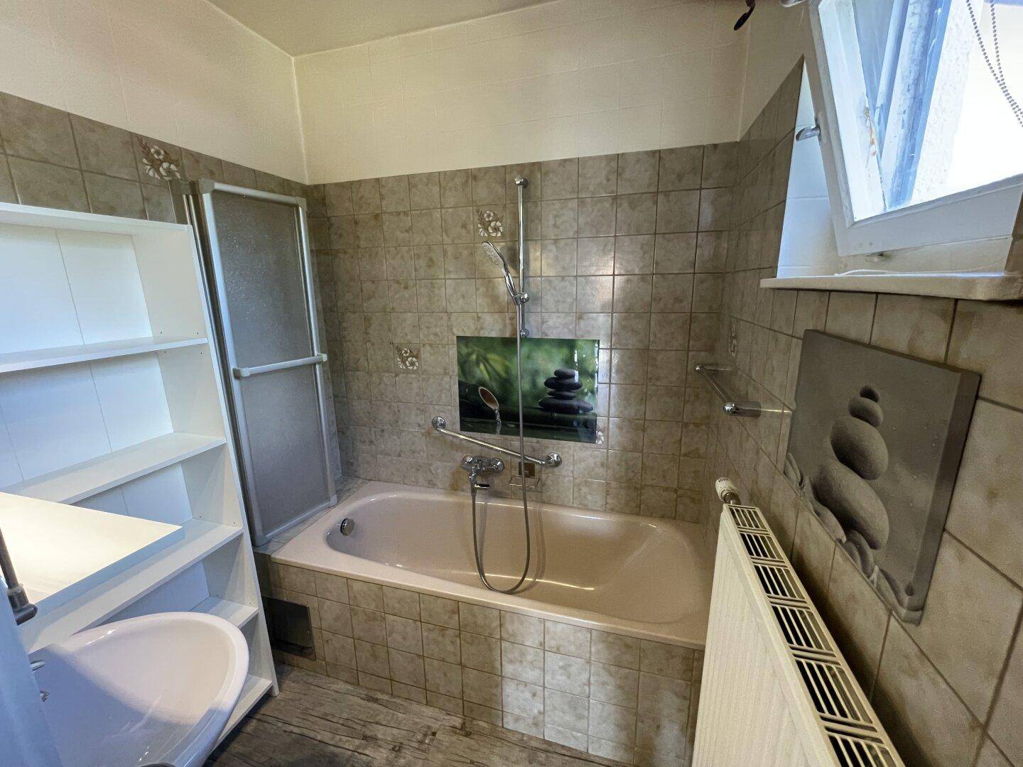 Badezimmer mit Badewanne, Duschabtrennung, Fliesen und Fenster für Tageslicht.
