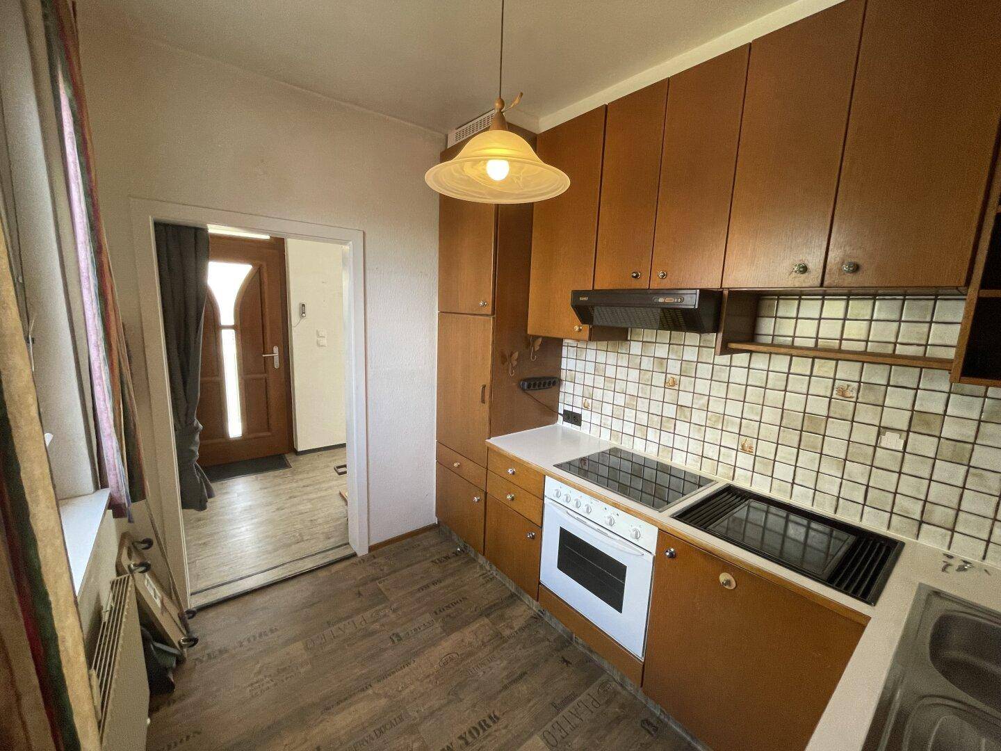Praktische Küche mit Holzfronten, Kochfeld und Zugang zum Eingangsbereich.