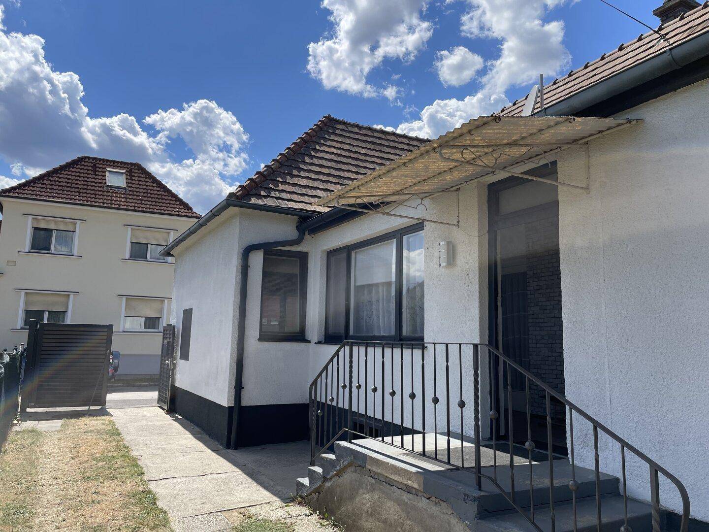 Eingangsbereich des Hauses mit Treppe und Vordach, umgeben von Grünflächen.