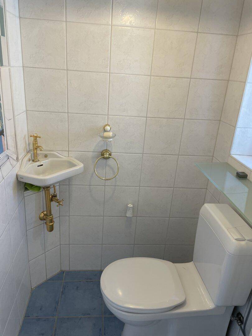Kleines Gäste-WC mit Fliesenboden, Eckwaschbecken und Toilette.