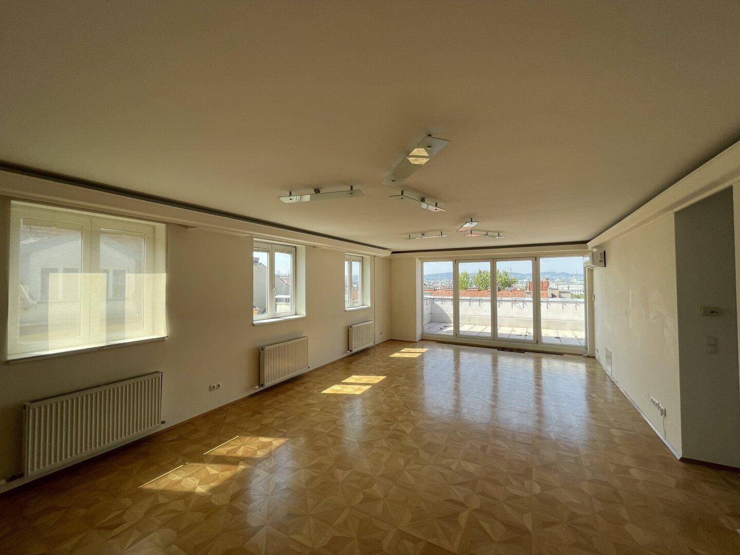Heller Wohnraum mit Parkettboden, großen Fenstern und viel natürlichem Licht.