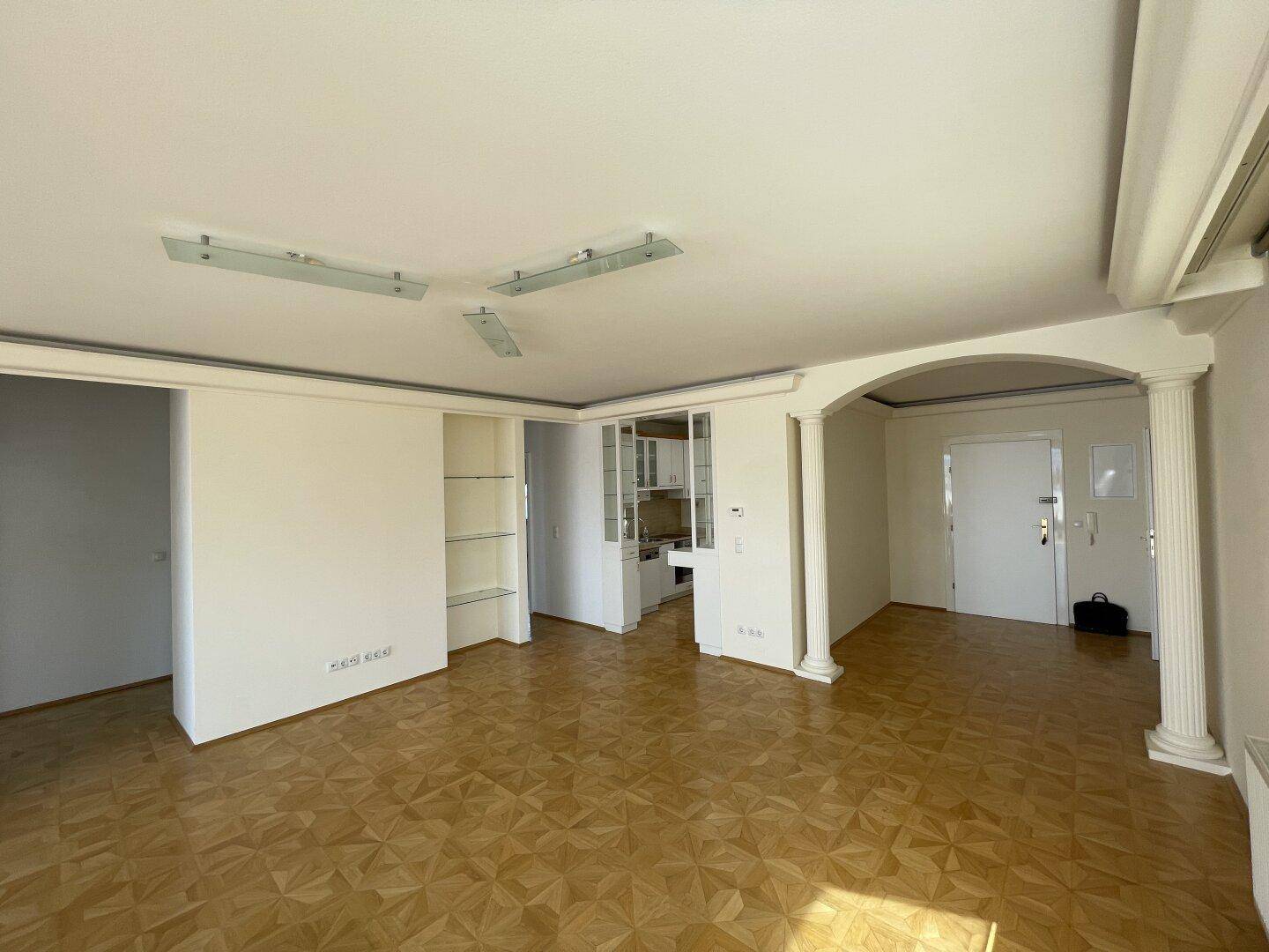 Wohnbereich mit Parkettboden, dekorativen Säulen und Blick in einen angrenzenden Raum.