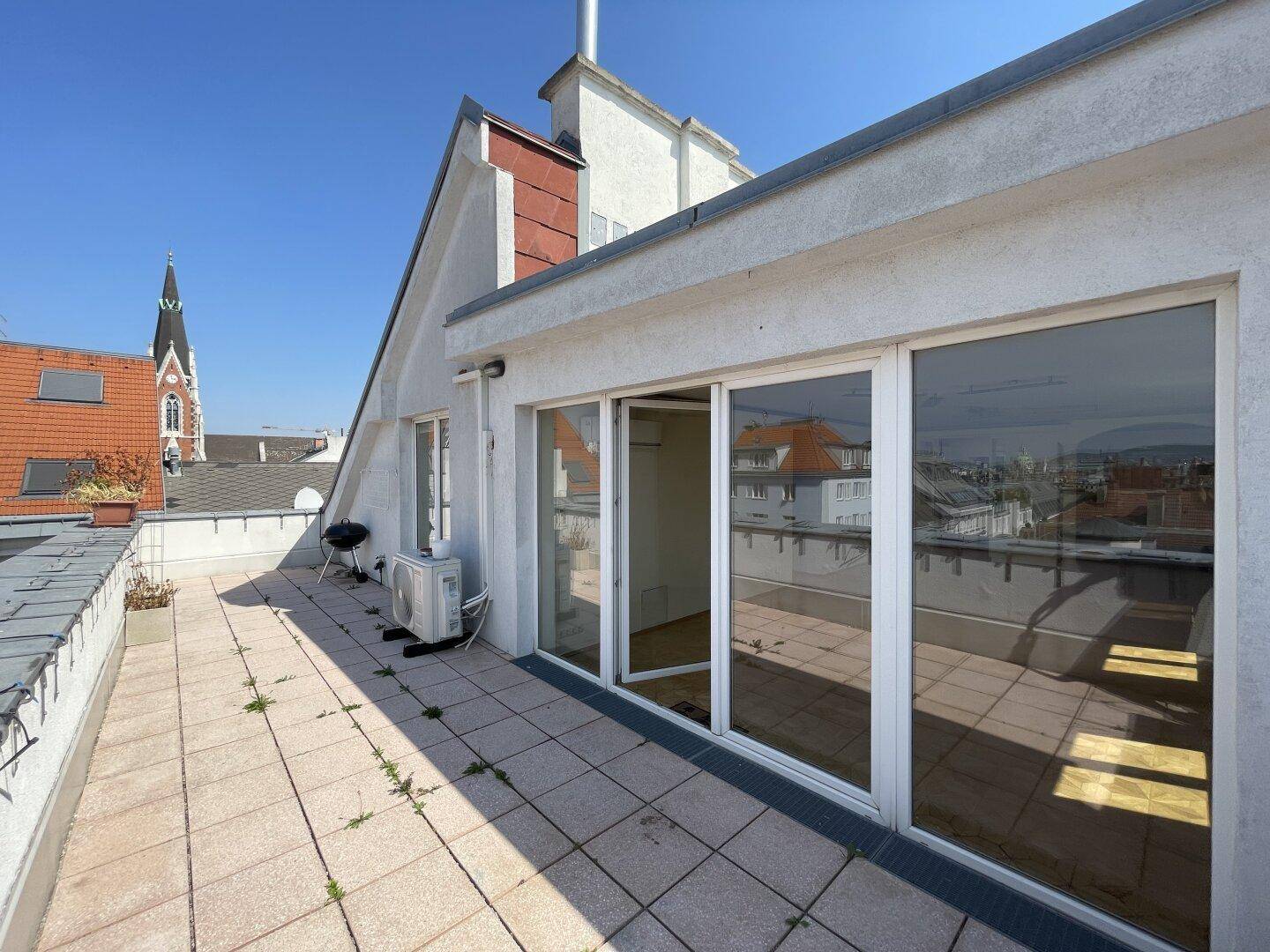 Geräumige Dachterrasse mit Fliesenboden und Zugang zu den Innenräumen durch große Glasfronten.