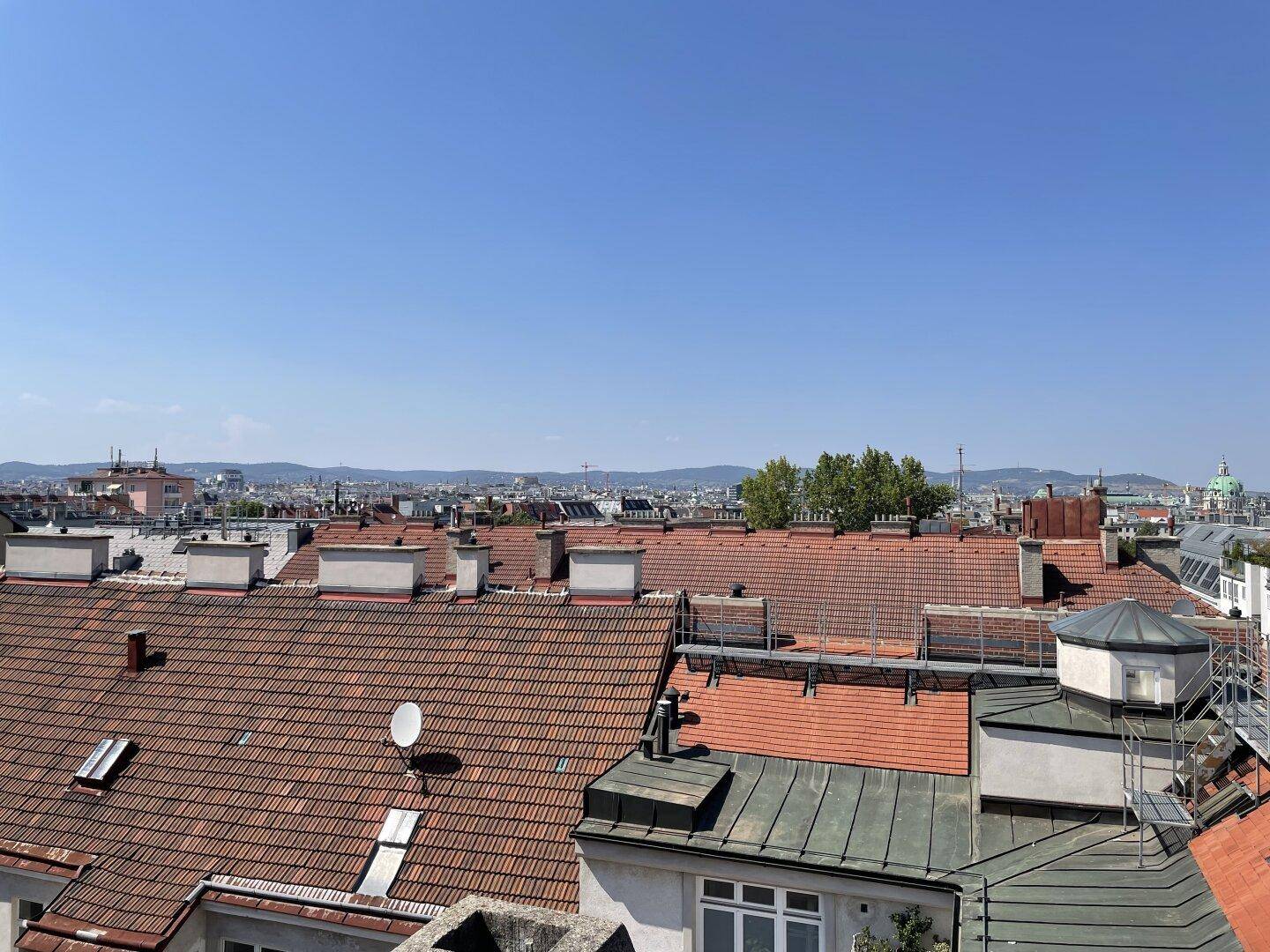 Weitläufiger Blick über die Dächer der Stadt mit historischen Gebäuden und Bergen im Hintergrund.