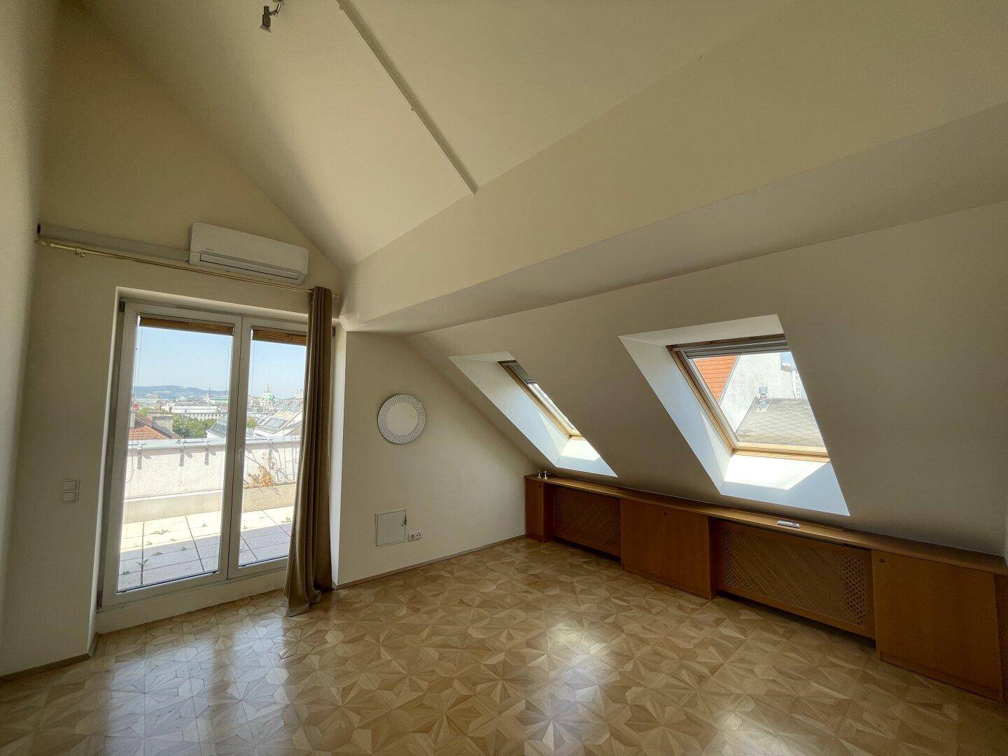 Schlafzimmer im Dachgeschoss mit Parkettboden, Dachfenstern und Zugang zur Terrasse.
