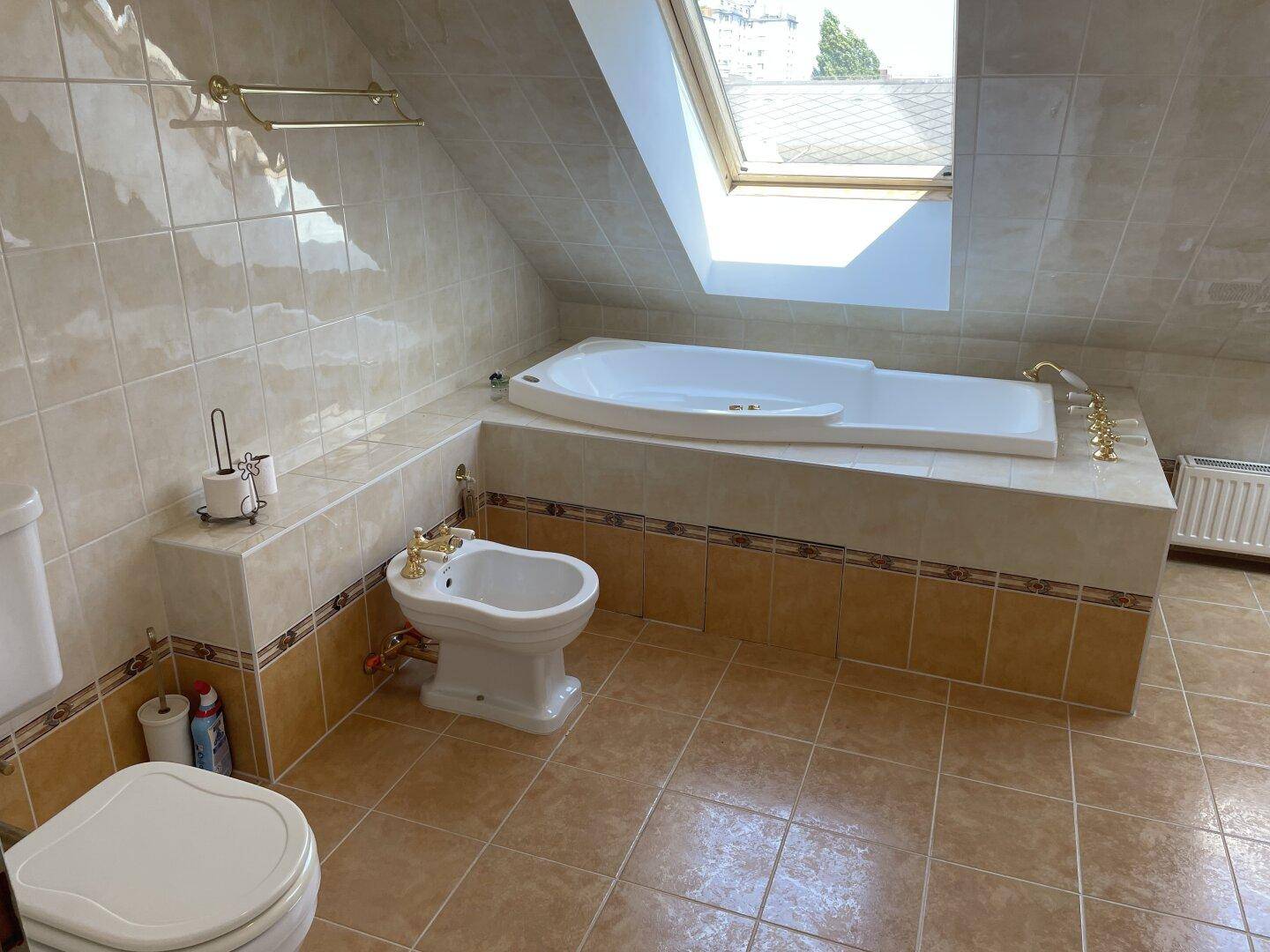 Gefliestes Badezimmer im Dachgeschoss mit Badewanne, Bidet und Dachfenster.
