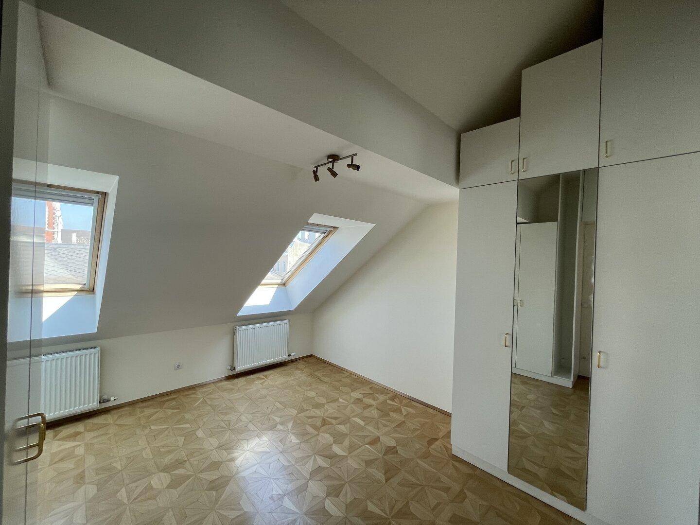 Helles Schlafzimmer im Dachgeschoss mit Parkettboden, Heizkörper und Dachfenster.