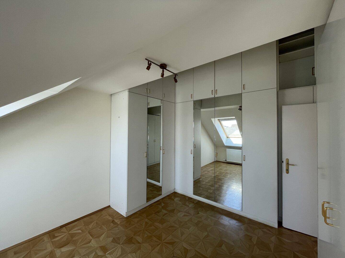 Schlafzimmer im Dachgeschoss mit Parkettboden, Einbauschränken und Dachfenster.