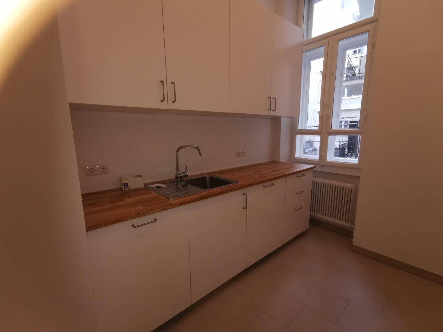 Funktionale Küchenzeile mit weißen Schränken, Holz-Arbeitsplatte und einem Fenster, das Tageslicht spendet.