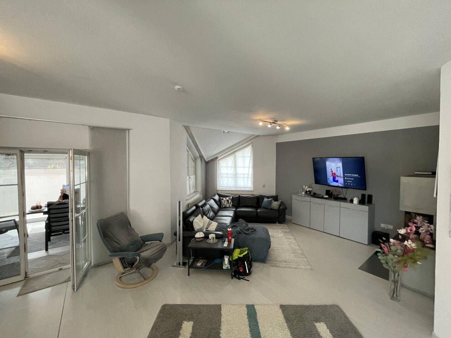 Gemütliches Wohnzimmer mit großem Ecksofa, Fernseher und Zugang zu einem Wintergarten.